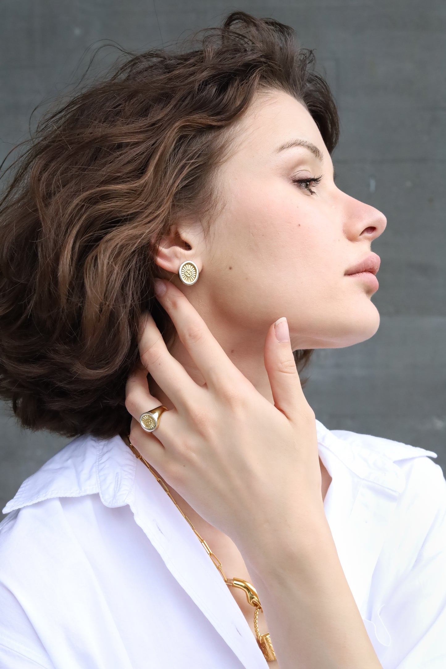Woman wearing gold earrings and a ring, with a neutral background