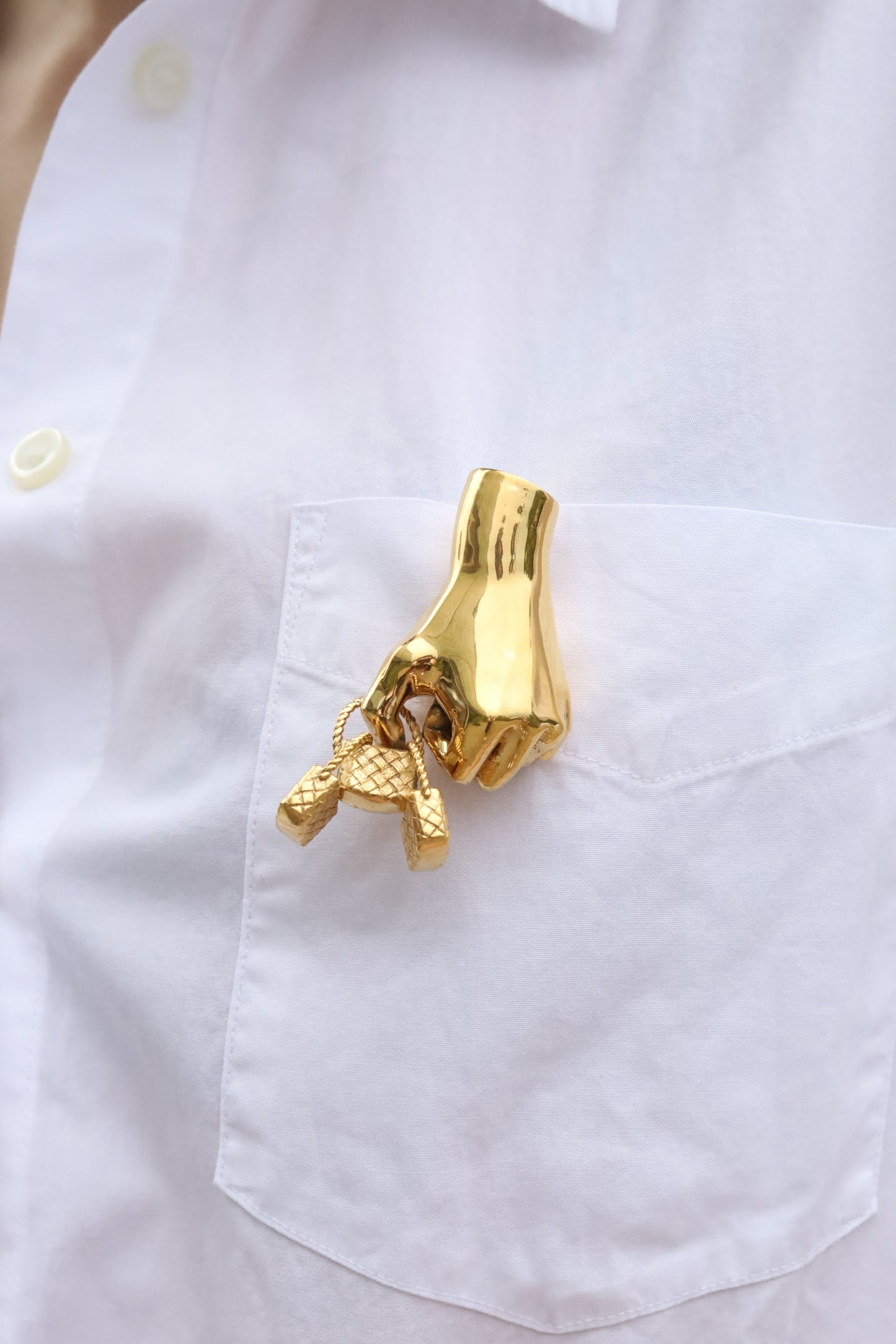Gold brooch shaped like a hand with a key on a white shirt