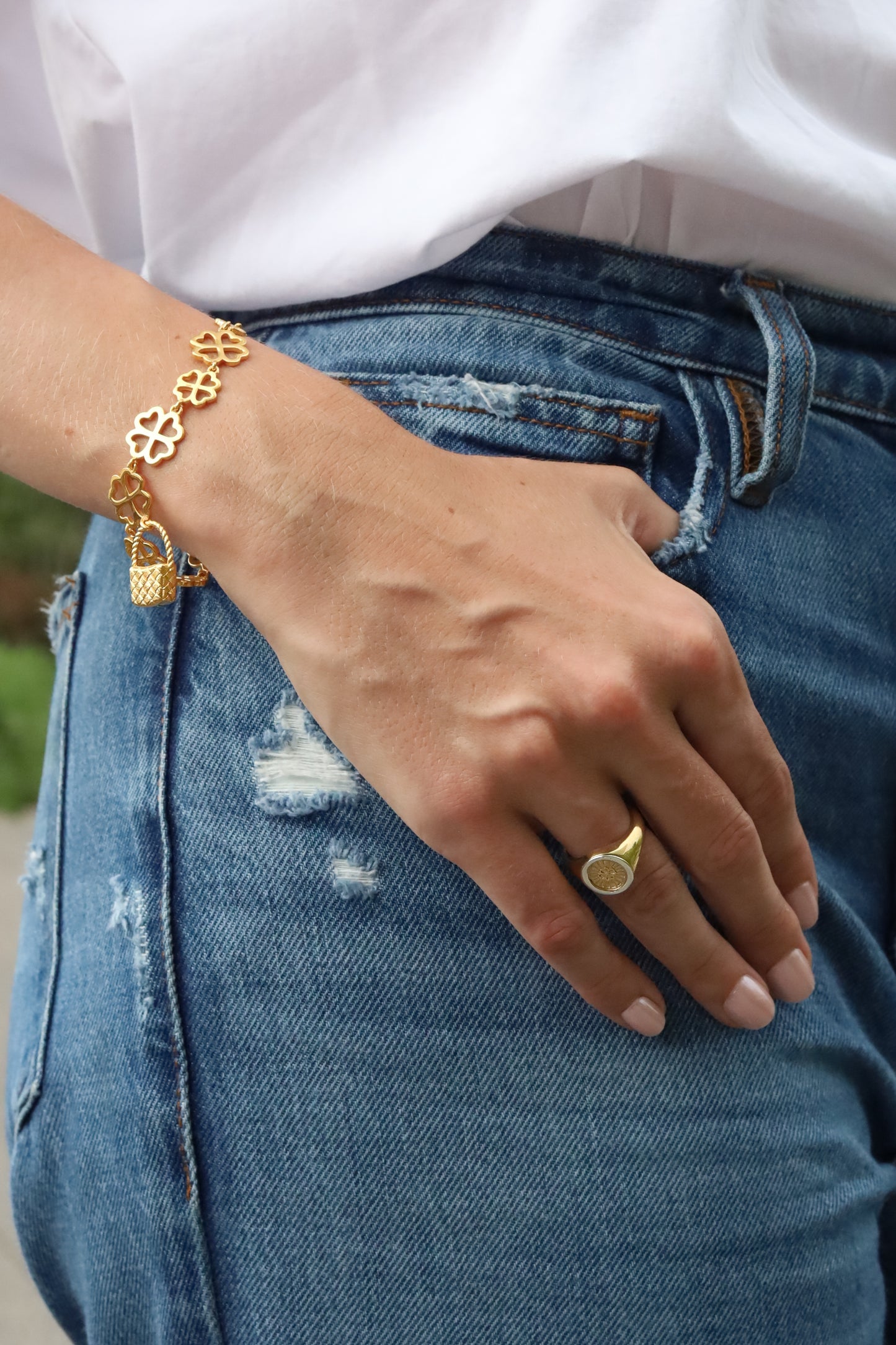 Hand wearing a gold bracelet and ring on blue jeans with a blurred background