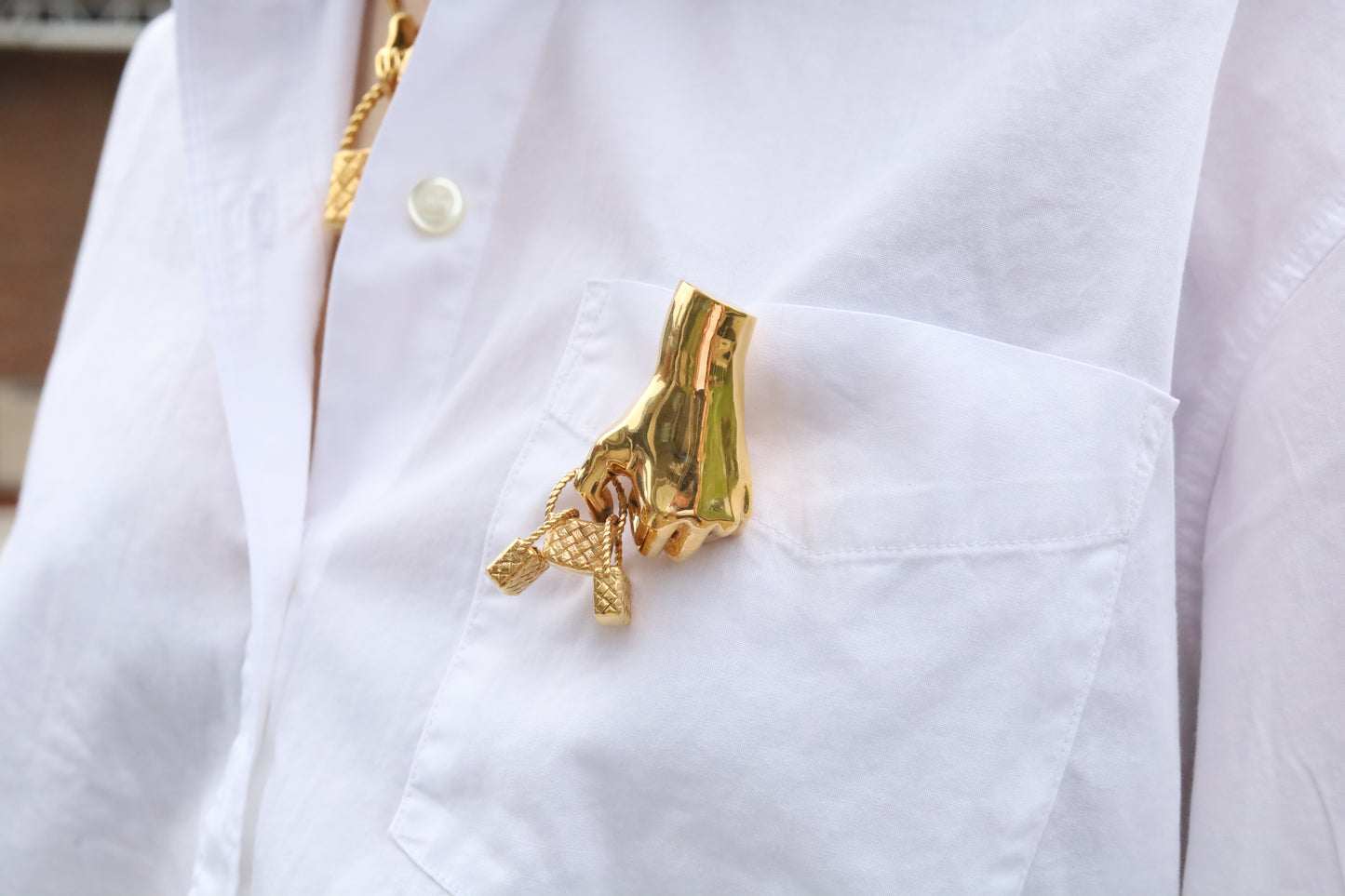 Gold hand-shaped brooch holding three baskets on a white shirt
