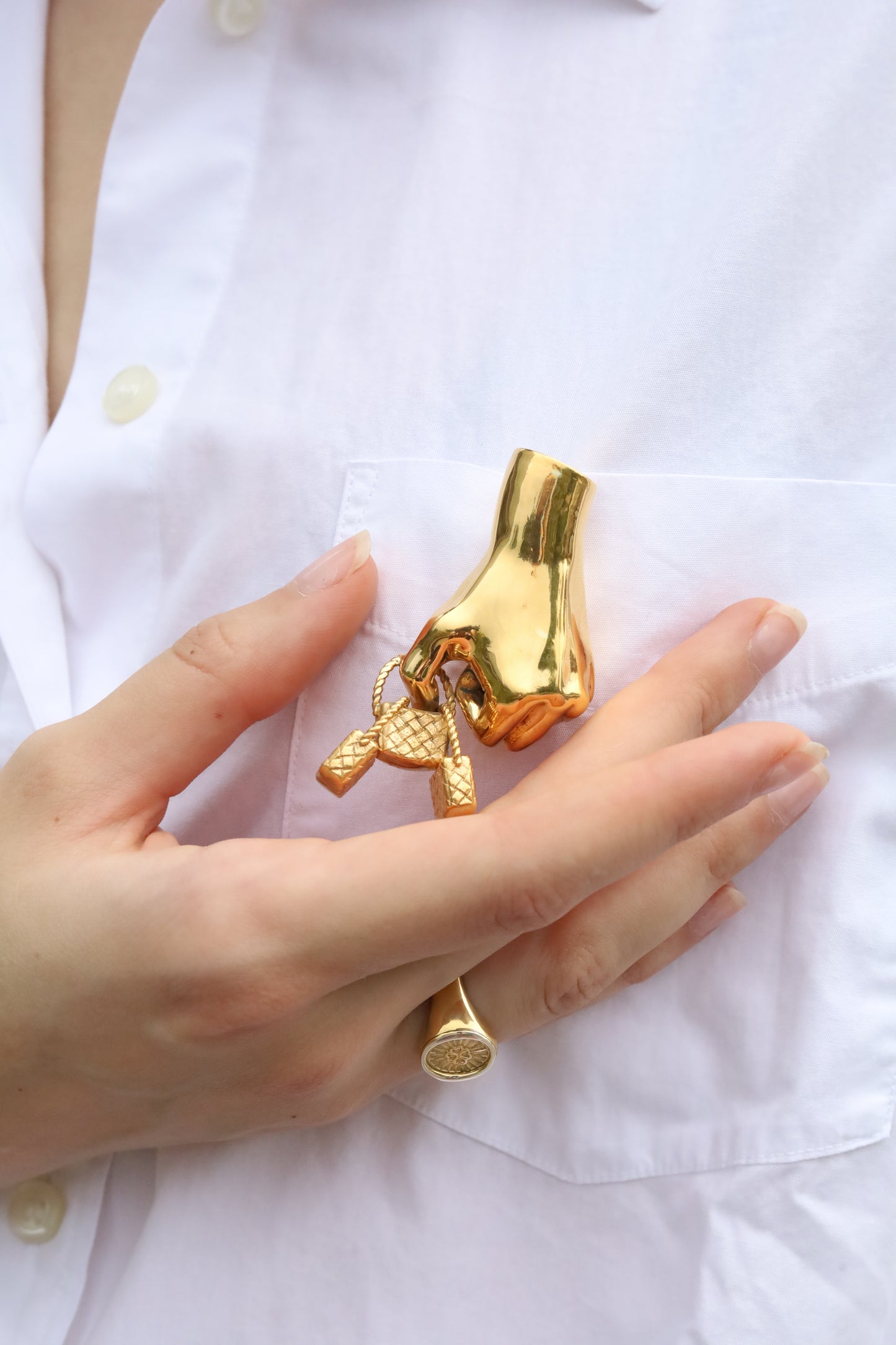 Gold brooch resembling a hand holding three baskets on a white shirt