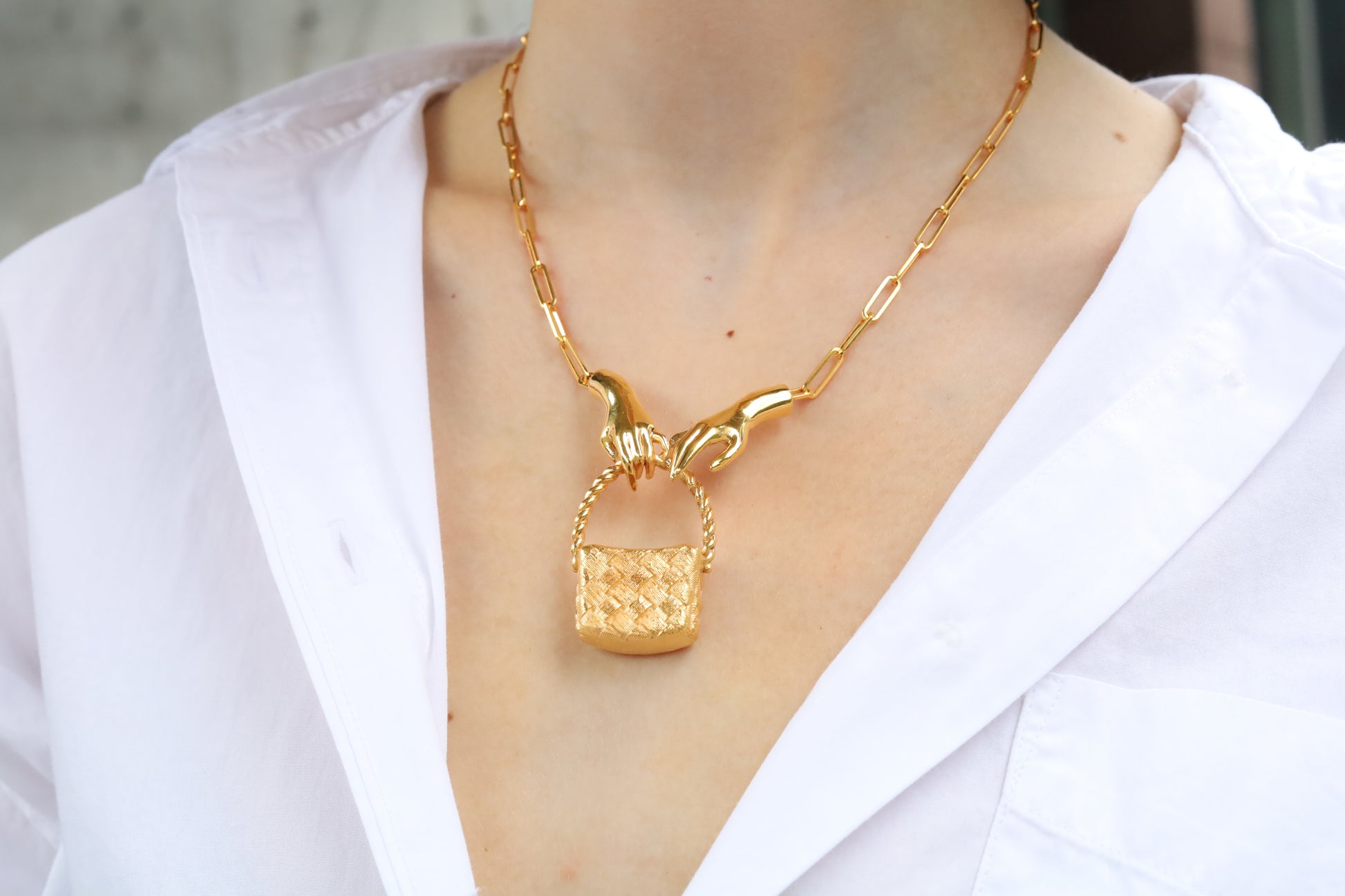 Gold necklace with a unique pendant worn by a person in a white shirt.