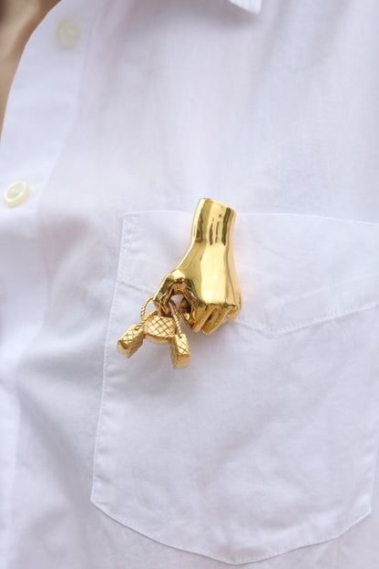 Gold brooch shaped like a hand with a key on a white shirt