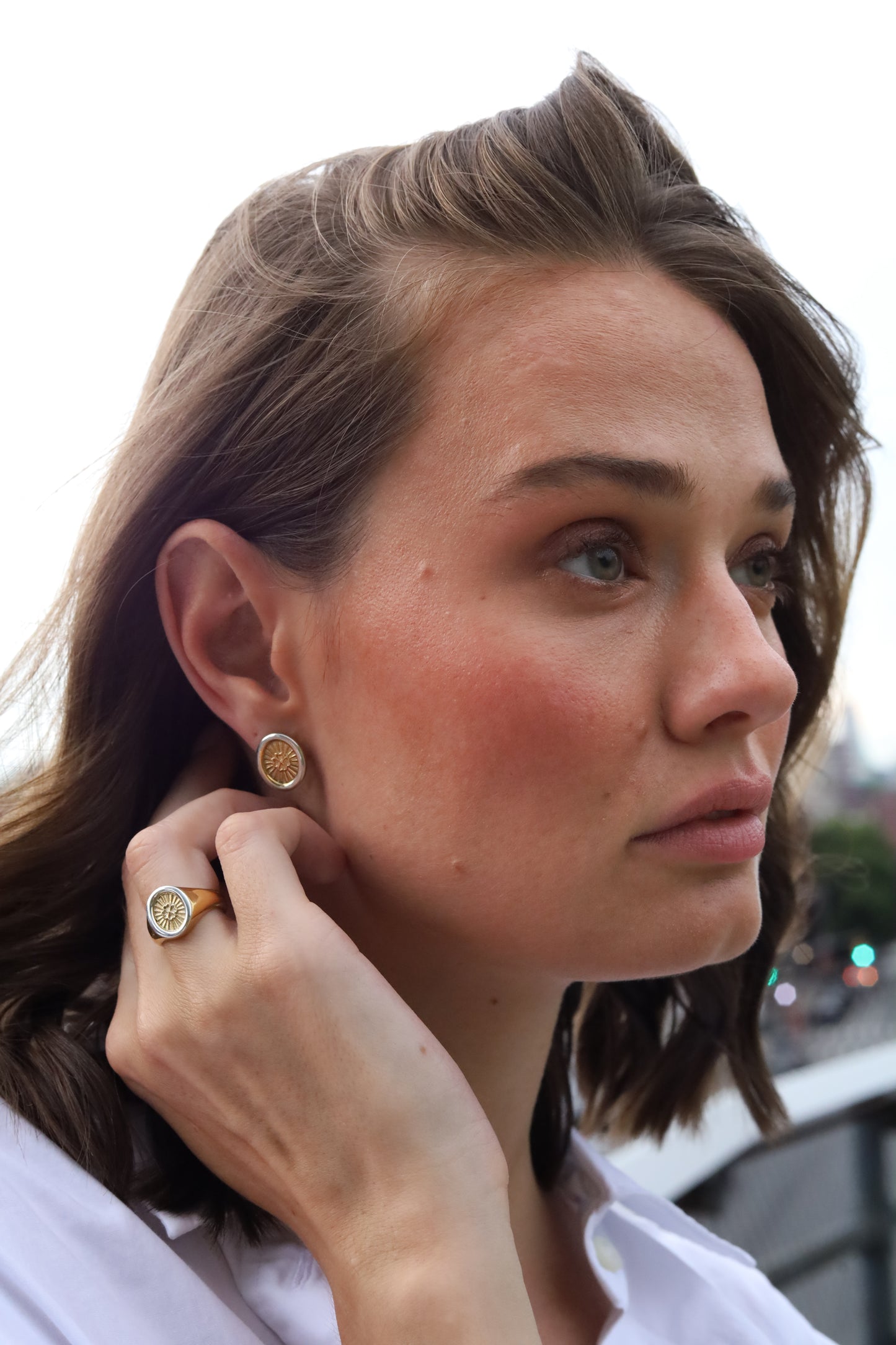 Woman adjusting her Jenna London earring with a blurred background