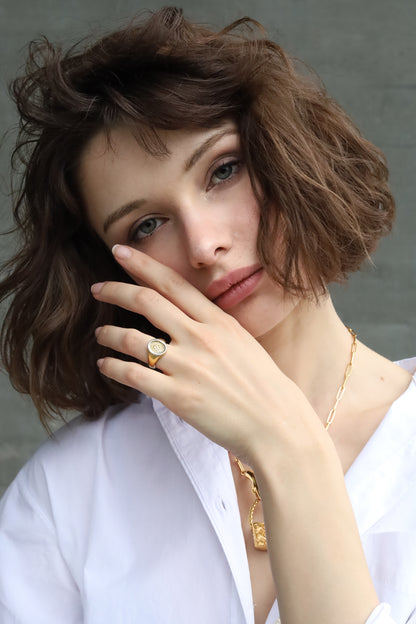 Woman with short brown hair wearing a gold Jenna London ring and necklace against a neutral background