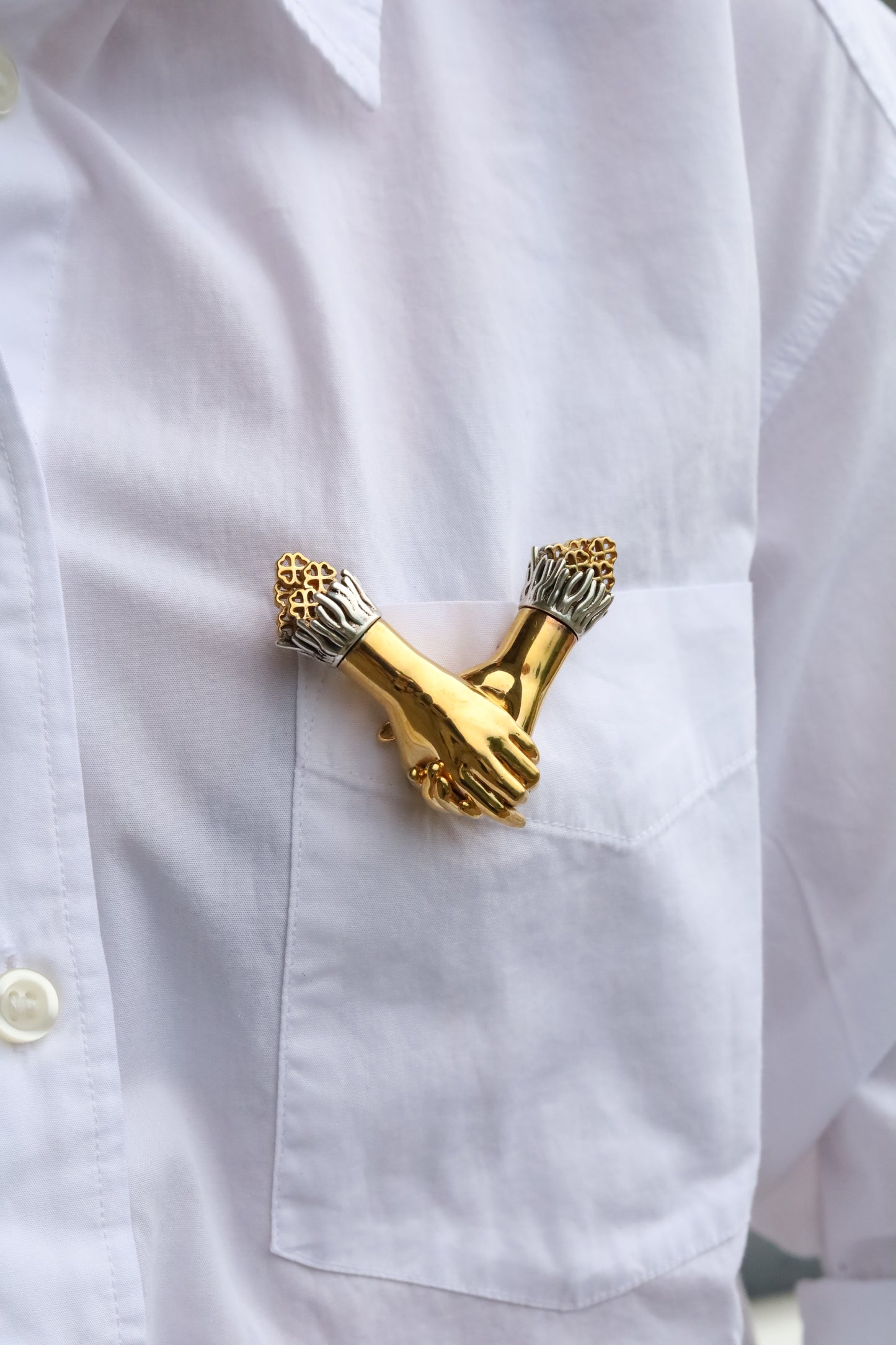 Jenna London Gold brooch shaped like two interlocked hands on a white shirt