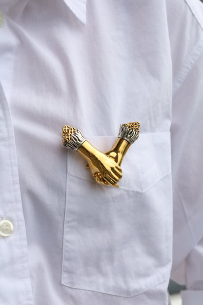 Jenna London Gold brooch shaped like two interlocked hands on a white shirt