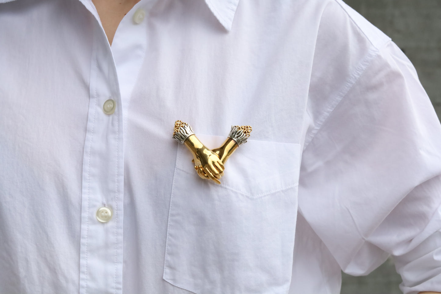 Woman wearing white shirt with a gold Jenna London brooch on a neutral background