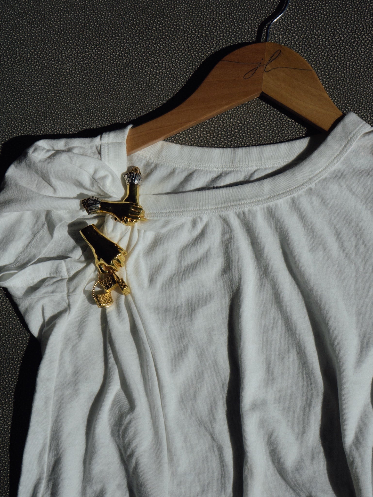White top with gold accents on a hanger against a dark textured background